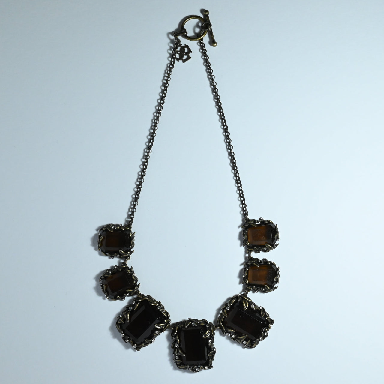 Large oblong brown resin necklace set in bronze plated metal with an organic theme offset with clear rhinestones. toggle clasp